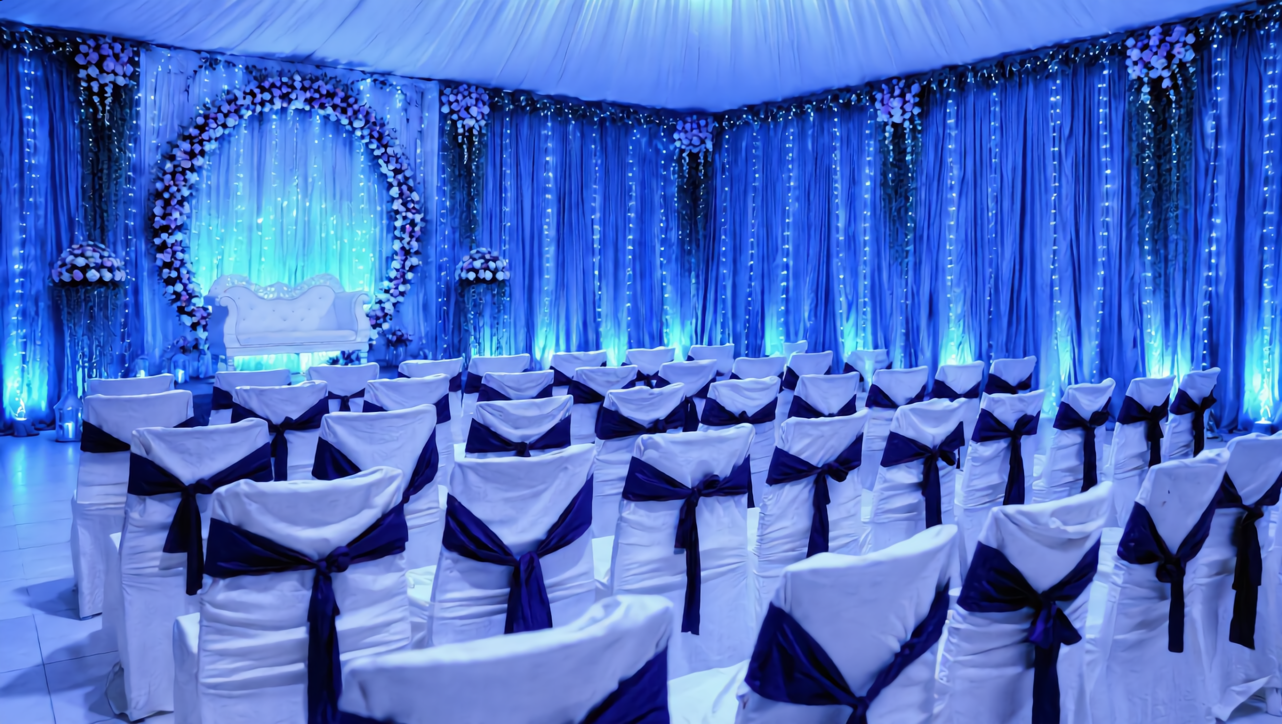 NS Convention hall lit in blue with white chairs and a floral-ring stage
